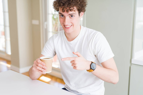 Jeune homme buvant emporter tasse de café à la maison très heureux pointant avec la main et le doigt
 - Photo, image