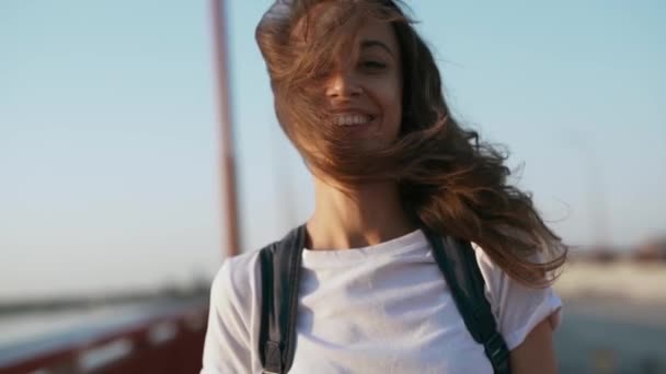 felice gioioso sorridente giovane bella donna in t-shirt bianca è in piedi sul ponte su sfondo cielo blu, ridendo, godendo tranquillo tramonto e guardando la fotocamera
. - Filmati, video