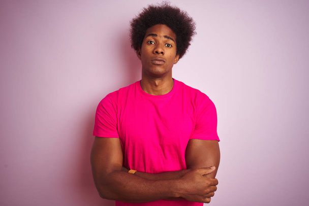 Fiatal amerikai férfi afro hajjal visel póló alatt álló elszigetelt rózsaszín háttér szkeptikus és ideges, disjóváhagyásáról kifejezés arcon a keresztezett fegyver. Negativ személy. - Fotó, kép