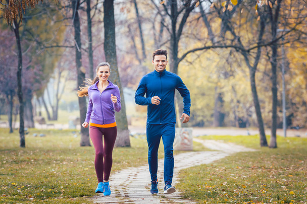 Woman and man running in autumn park for sport - Foto, afbeelding