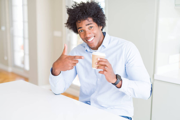 アフロヘアを持つアフリカ系アメリカ人男性は、手と指で指し示すコーヒーのテイクアウトカップを飲む - 写真・画像