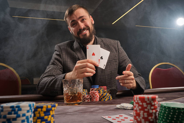 Красивый бородатый мужчина играет в покер, сидя за столом в казино
. - Фото, изображение