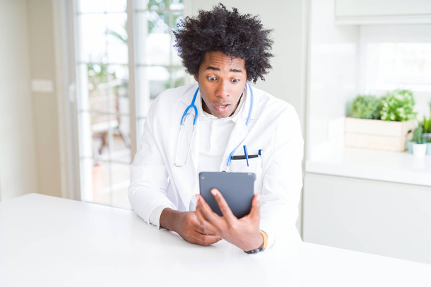 African American doctor man using tablet at the clinic scared in shock with a surprise face, afraid and excited with fear expression - Photo, Image