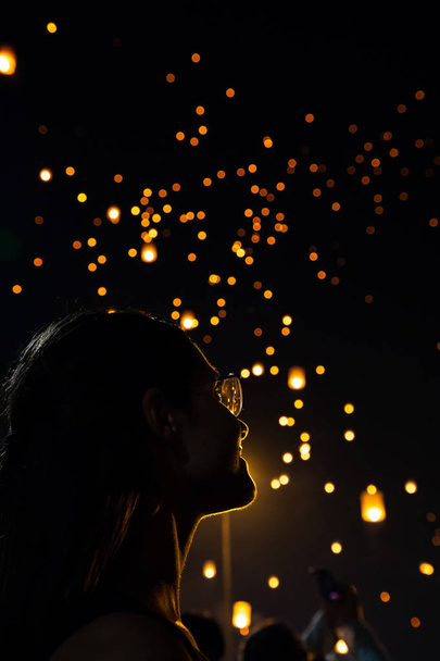 Beautiful woman silhouett portrait looking at Loy Krathong paper lanterns as bokeh on background in Thailand - Photo, Image