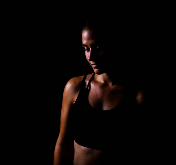 Chica en ropa deportiva mirando hacia abajo aislado con fondo negro l
 - Foto, imagen