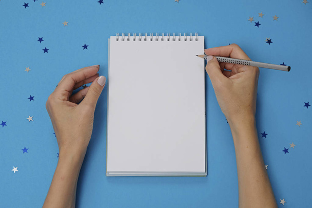Blank notebook and female hands with pencil on festive blue background with stars - Фото, изображение