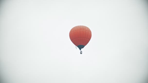 Un globo aerostático naranja volando sobre un fondo de cielo nublado blanco
 - Metraje, vídeo