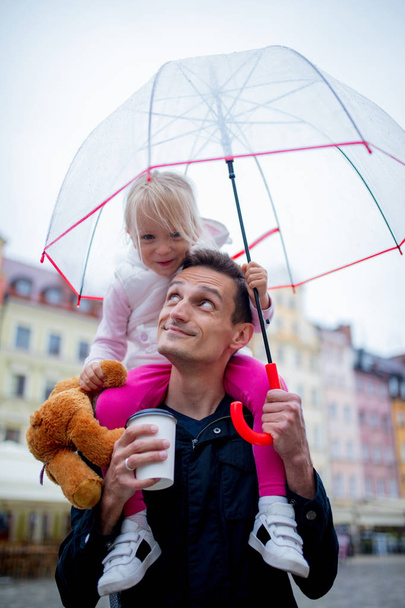 μικρό κορίτσι με ομπρέλα κάθεται στους ώμους του πατέρα της - Φωτογραφία, εικόνα