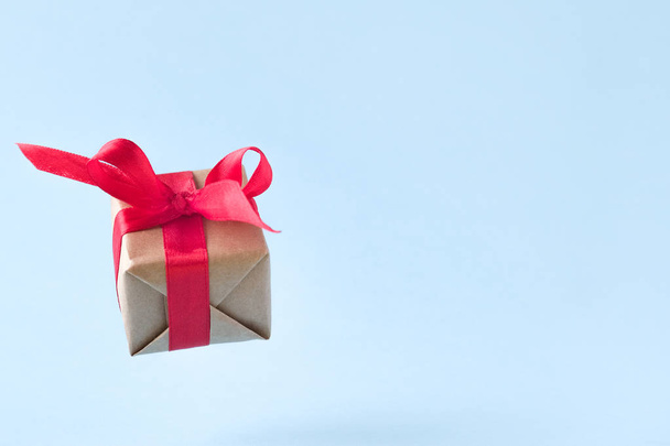 Gift box with red ribbon on blue background. zero gravity. levitation. milimalism. copyspace. Concept sales, shopping, christmas holidays and birthday - Φωτογραφία, εικόνα