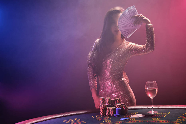 Brunette meisje met een perfecte kapsel en heldere make-up poseert met fan van honderd dollar biljetten in haar handen. Casino, poker. - Foto, afbeelding