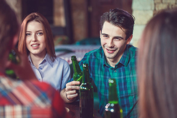 Amigos tomando uma bebida em um bar, Eles estão sentados em uma mesa de madeira com cervejas e pizza
 - Foto, Imagem