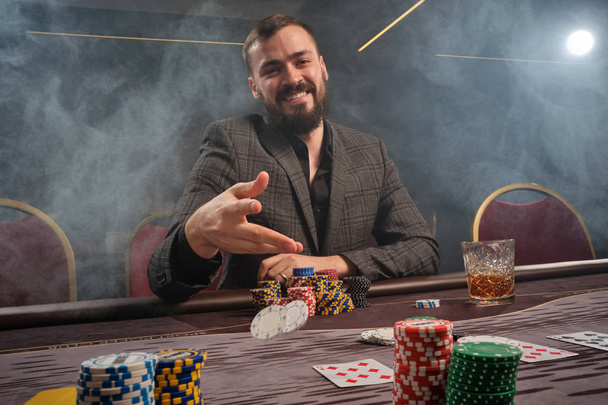 Handsome bearded man is playing poker sitting at the table in casino. - Photo, Image