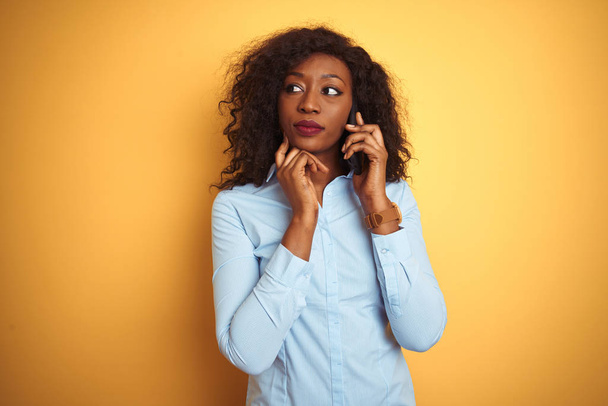 Jeune femme afro-américaine parlant sur le smartphone sur fond jaune isolé sérieux visage réfléchissant à la question, idée très confuse
 - Photo, image