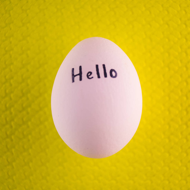 White chicken egg with black inscription hello on a yellow background. - Photo, Image