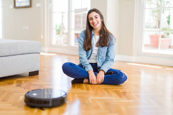 自動掃除機を使って床をきれいにし、家事ロボットを制御する若い女性 - 写真・画像