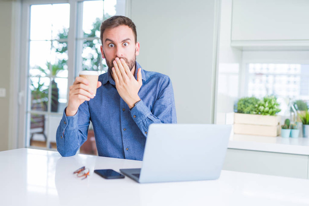 Bell'uomo che lavora con il computer portatile e beve una tazza di caffè coprire la bocca con la mano scioccato dalla vergogna per errore, espressione di paura, spaventato in silenzio, concetto segreto
 - Foto, immagini