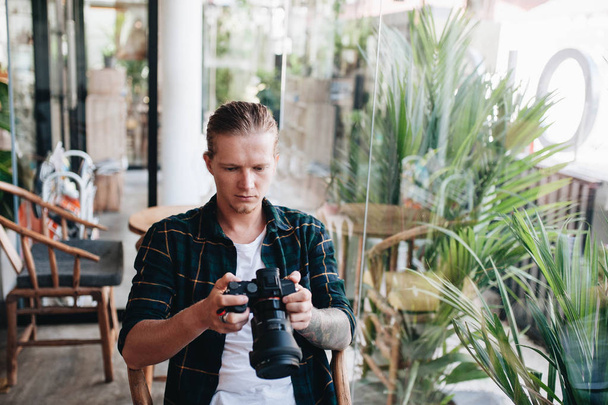 Creative photographer holding professional camera, sitting at cafe with laptop. - Photo, Image