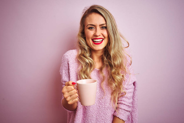 junge schöne Frau trägt Pullover, trinkt eine Tasse Kaffee über rosa isolierten Hintergrund mit einem glücklichen Gesicht stehend und lächelnd mit einem selbstbewussten Lächeln Zähne zeigen - Foto, Bild