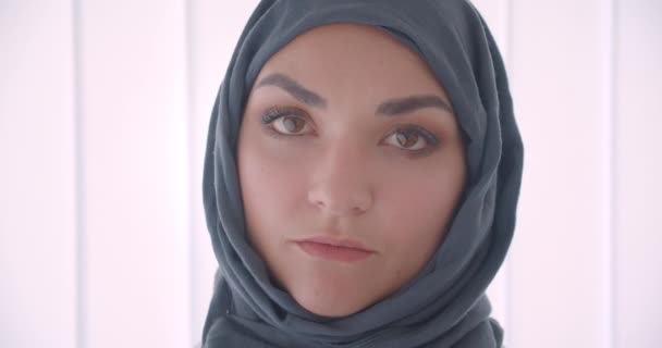Closeup portrait of young arabian attractive businesswoman in hijab looking at camera in the white apartment indoors - Filmati, video