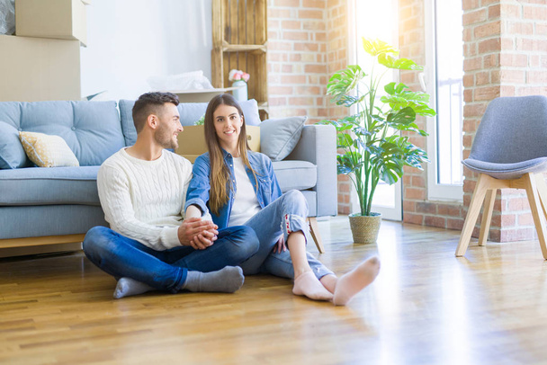 Young beautiful couple sitting on the floor of new apartment, smiling in love happy for moving to a new home - Foto, immagini