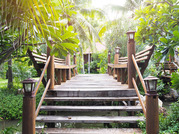Ponte de madeira que cruza o canal pequeno na decoração verde do jardim. Caminho de madeira no resort tropical
. - Foto, Imagem