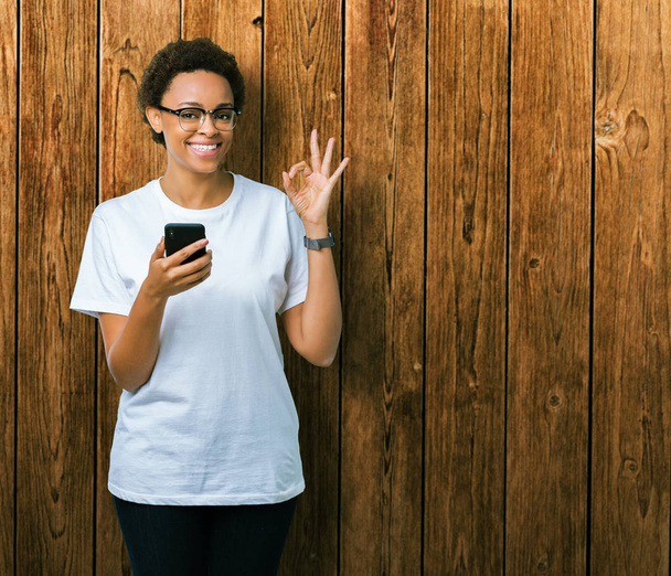 Jeune femme afro-américaine utilisant un smartphone sur fond isolé faisant signe ok avec les doigts, excellent symbole
 - Photo, image