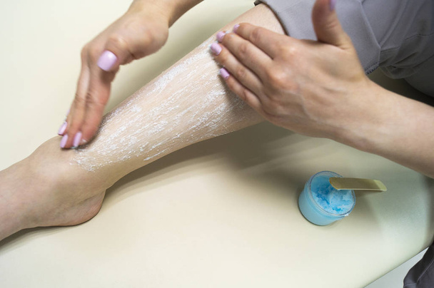 Rejuvenation procedure. The girl puts a blue scrub on her leg - Foto, Imagem
