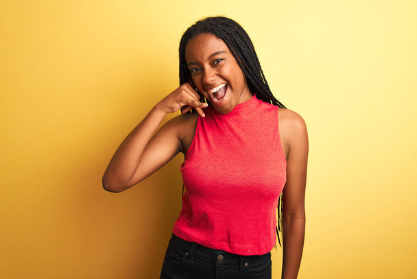 Afrikkalainen amerikkalainen nainen yllään punainen rento t-paita seisoo yli eristetty keltainen tausta hymyillen tekee puhelimen ele käsin ja sormin kuin puhua puhelimessa. Käsitteiden ilmoittaminen
. - Valokuva, kuva