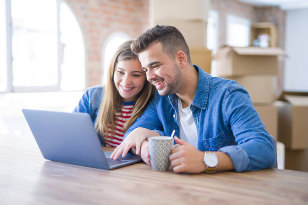 junges Paar entspannt einen Kaffee trinkend und den Computer-Laptop um Kartons herum benutzend, sehr glücklich beim Umzug in ein neues Haus - Foto, Bild