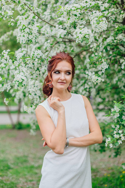 Charming woman wearing beautiful white dress under the apple tree - Фото, зображення