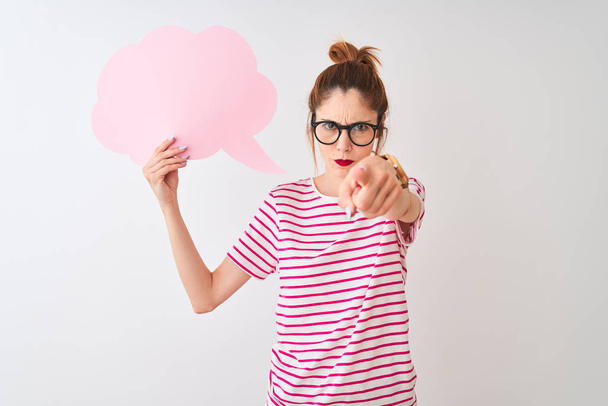 Κοκκινομάλλα γυναίκα φορώντας γυαλιά κρατώντας σύννεφο ομιλία φούσκα πάνω από απομονωμένο λευκό φόντο που οδηγεί με το δάχτυλο στην κάμερα και σε σας, σημάδι χεριού, θετική και αυτοπεποίθηση χειρονομία από το μέτωπο - Φωτογραφία, εικόνα
