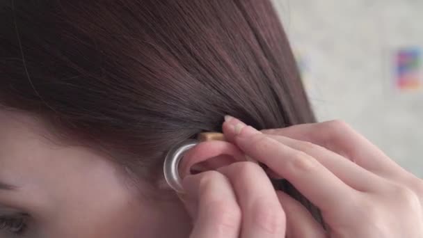jovem mulher insere um aparelho auditivo em seu ouvido de perto
 - Filmagem, Vídeo