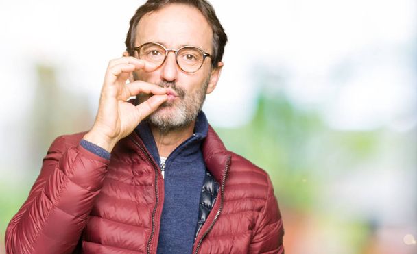 Middle age handsome man wearing glasses and winter coat mouth and lips shut as zip with fingers. Secret and silent, taboo talking - Fotoğraf, Görsel