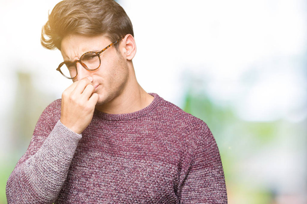 Mladý pohledný muž nosí brýle nad izolované pozadí vonící něco smradlavá a nechutné, nesnesitelný zápach, držení dech s prsty na nos. Pachy koncept. - Fotografie, Obrázek