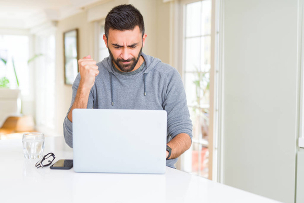 Pohledný Hispánec pracující s počítačovým laptopem rozčilené a frustrovaný pokřikem hněvu, šílený a křičící s zvedanou rukou, koncept hněvu - Fotografie, Obrázek