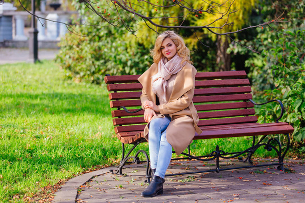 Young beautiful woman sitting on the bench in autumn park - Foto, Imagen