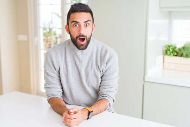 Handsome hispanic man wearing casual sweater at home afraid and shocked with surprise expression, fear and excited face. - Foto, Imagen