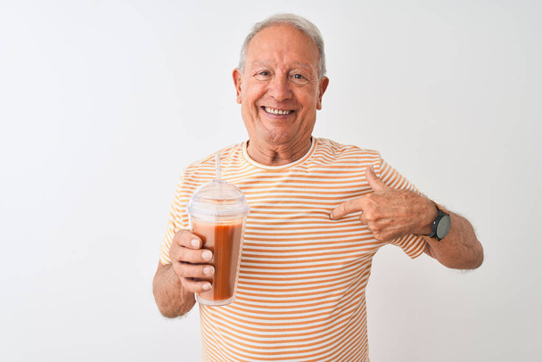 Uomo anziano che indossa t-shirt a righe bere frullato di pomodoro su sfondo bianco isolato con faccia a sorpresa puntando il dito verso se stesso
 - Foto, immagini