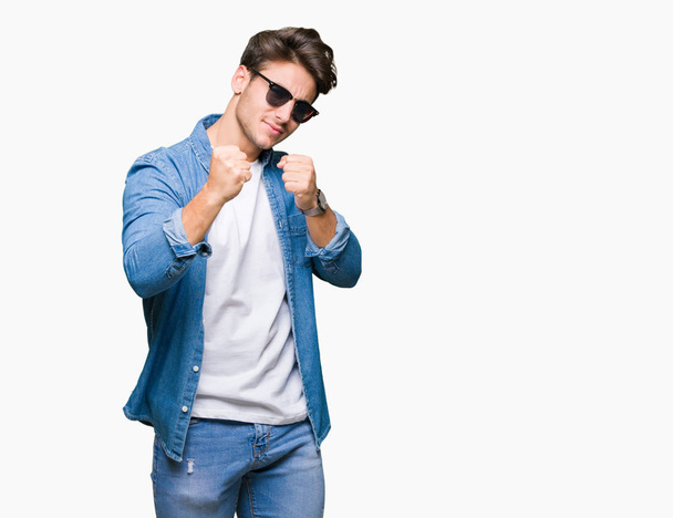 Молодой красивый мужчина в солнечных очках на изолированном фоне, готовый бороться с кулаком жеста защиты, сердитый и расстроенный лицо, боится проблем
 - Фото, изображение