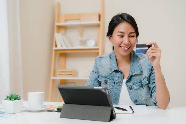 Beautiful smart business Asian woman using tablet buying online shopping by credit card while wear smart casual sitting on desk in living room at home. Lifestyle woman working at home concept. - Фото, изображение