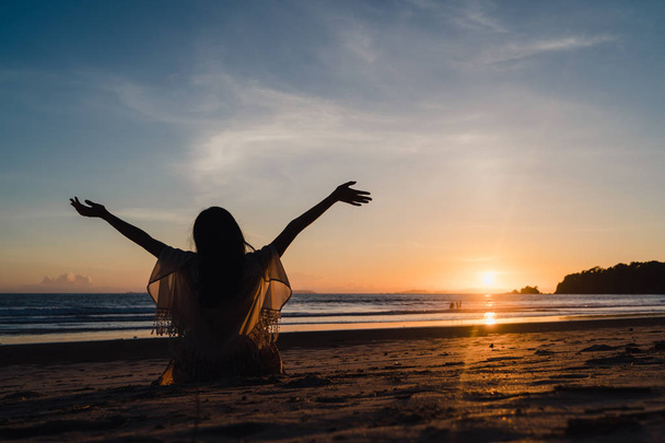 Молодая азиатка смотрит закат возле пляжа, красивая женщина счастливый расслабиться насладиться моментом, когда закат вечером. Жизнь женщины путешествовать по пляжной концепции
. - Фото, изображение