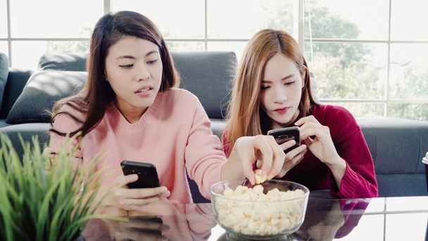Азіатські жінки за допомогою смартфона і їдять попкорн у вітальні на дому, Група сусід друг насолоджуватися смішні момент лежачи на дивані. Спосіб життя жінок розслабитися на дому концепції. - Фото, зображення