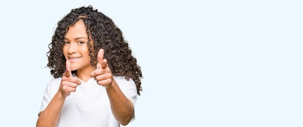 Young beautiful woman with curly hair wearing white t-shirt pointing fingers to camera with happy and funny face. Good energy and vibes. - Photo, Image