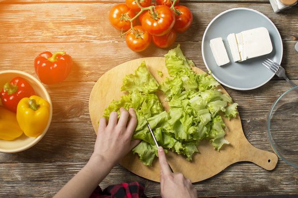 Hände des Mädchens schneiden Salat auf einem Tisch, eine Frau bereitet einen Gemüsesalat zu, gesundes Essen, ein Messer hackt Gemüse - Foto, Bild