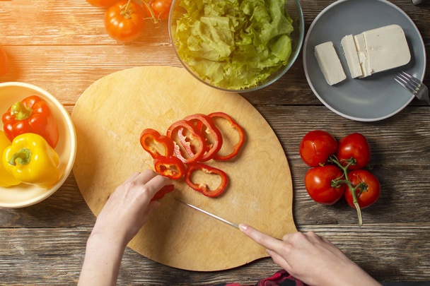 mãos de uma menina cortam pimentão de sino em uma mesa, o processo de fazer salada vegetariana, corte de close-up de verduras e verdes
 - Foto, Imagem
