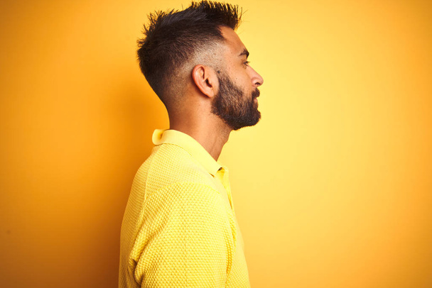 Молодий індійський чоловік у поло стоїть над ізольованим жовтим тлом, дивлячись в бік, розслабляє профільну позу з природним обличчям з впевненою посмішкою
. - Фото, зображення
