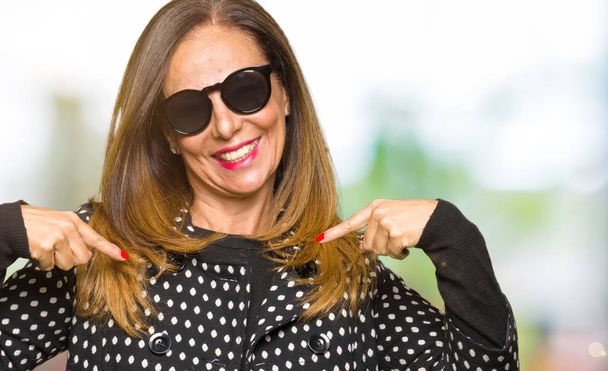 Beautiful middle age woman wearing sunglasses looking confident with smile on face, pointing oneself with fingers proud and happy. - Photo, Image
