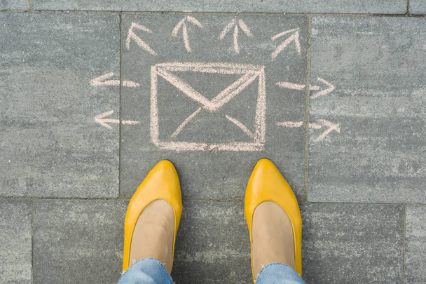 Female feet with abstract envelope message letter with arrows in different directions, written on grey sidewalk - Foto, imagen