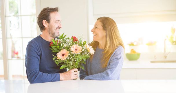 Romantische middenleeftijd paar houden van bloemen in liefde thuis - Foto, afbeelding