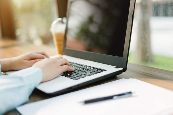 Крупный план бизнес-женщина работает с ноутбуком с чистым черным экраном сделать заметку документ и смартфон в кафе, как фон
. - Фото, изображение